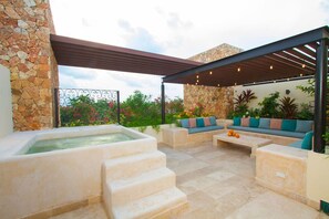 Une terrasse extérieure dotée d’un jacuzzi, de murs en pierre et de mobilier d’extérieur.