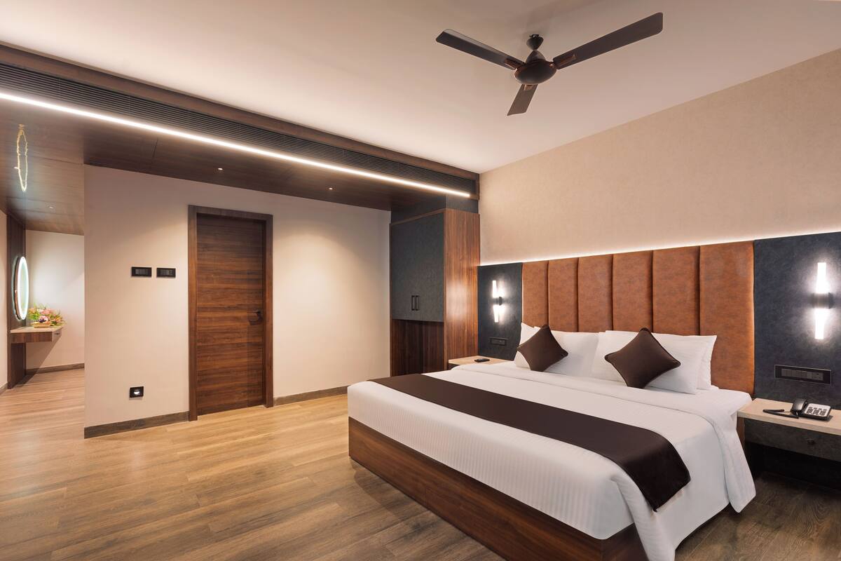 A modern hotel room with a large bed, wooden flooring, a ceiling fan, and a nightstand with a phone.