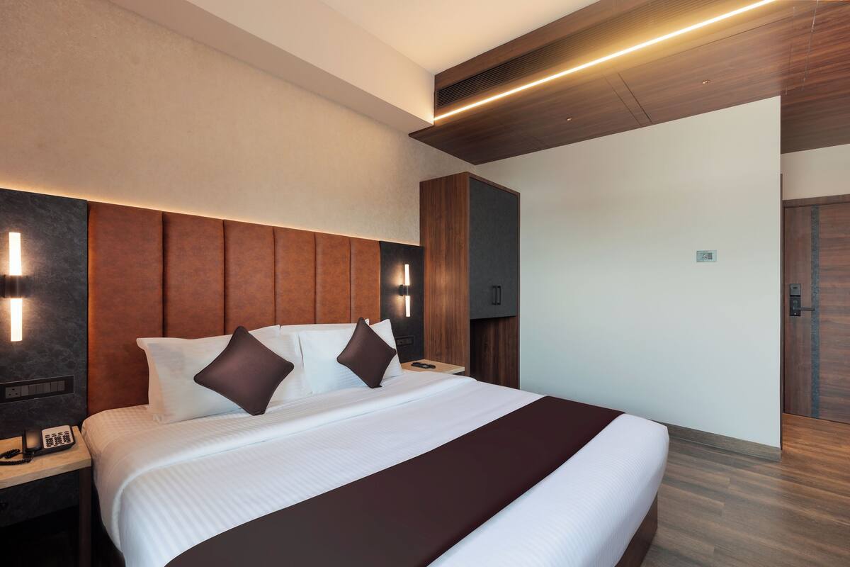 A modern hotel room with a large bed, wooden headboard, and built-in bedside tables.