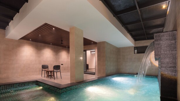Ein moderner Innenpoolbereich mit einem klaren Wasserspiel, Sitzgelegenheiten und einer Decke mit Holzpaneelen.