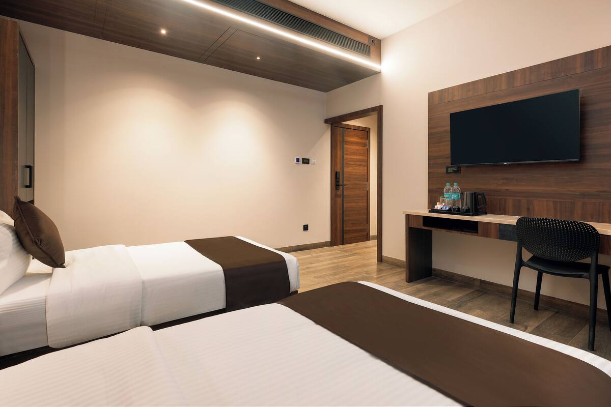 A hotel room with two beds, a desk, a chair, a flat-screen TV, and a wooden accent wall.