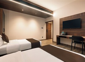 Habitación de hotel con dos camas, un escritorio, una silla, un televisor de pantalla plana y una pared decorativa de madera.