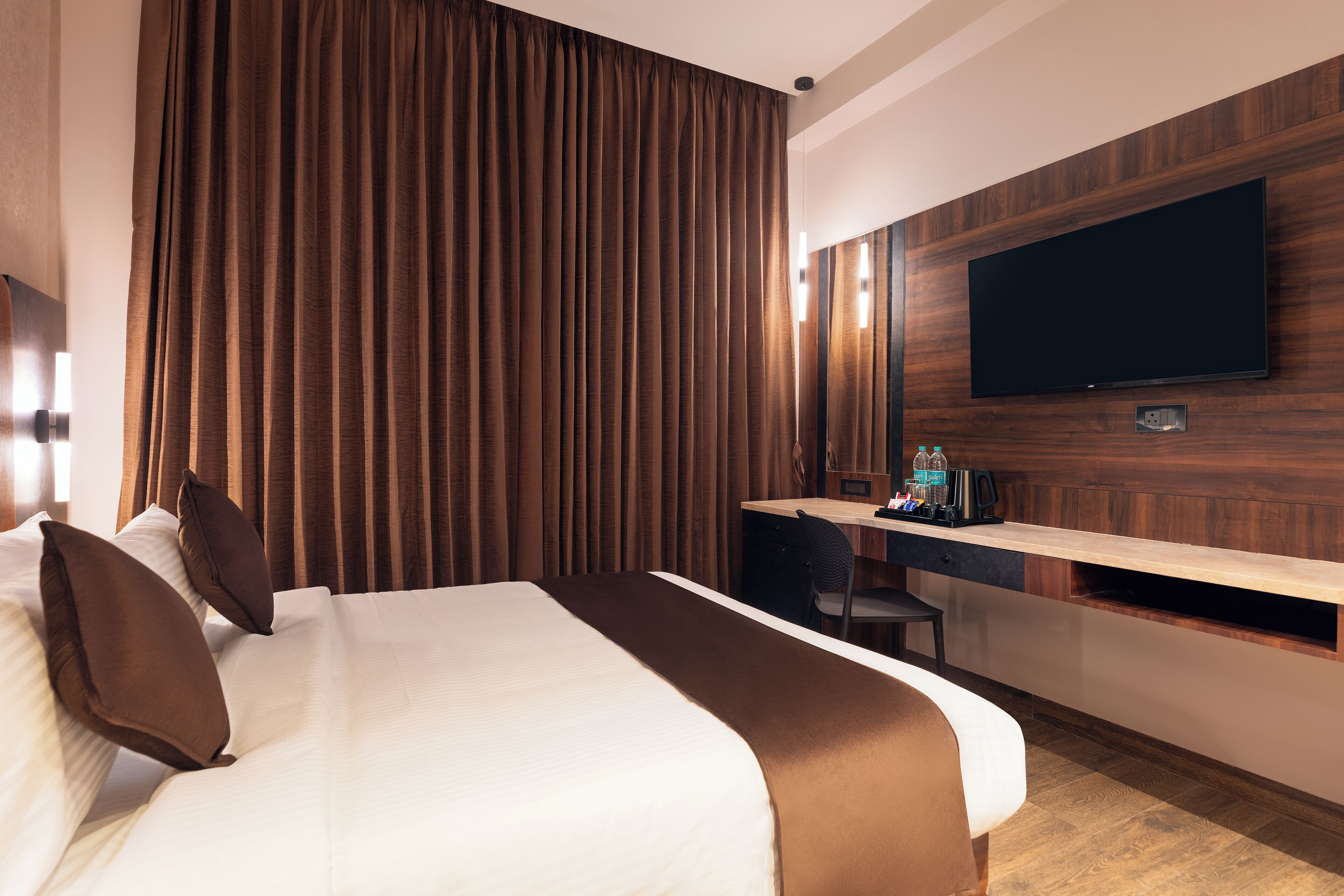 A modern hotel room with a large bed, a desk with a computer, and a flat-screen TV mounted on the wall.