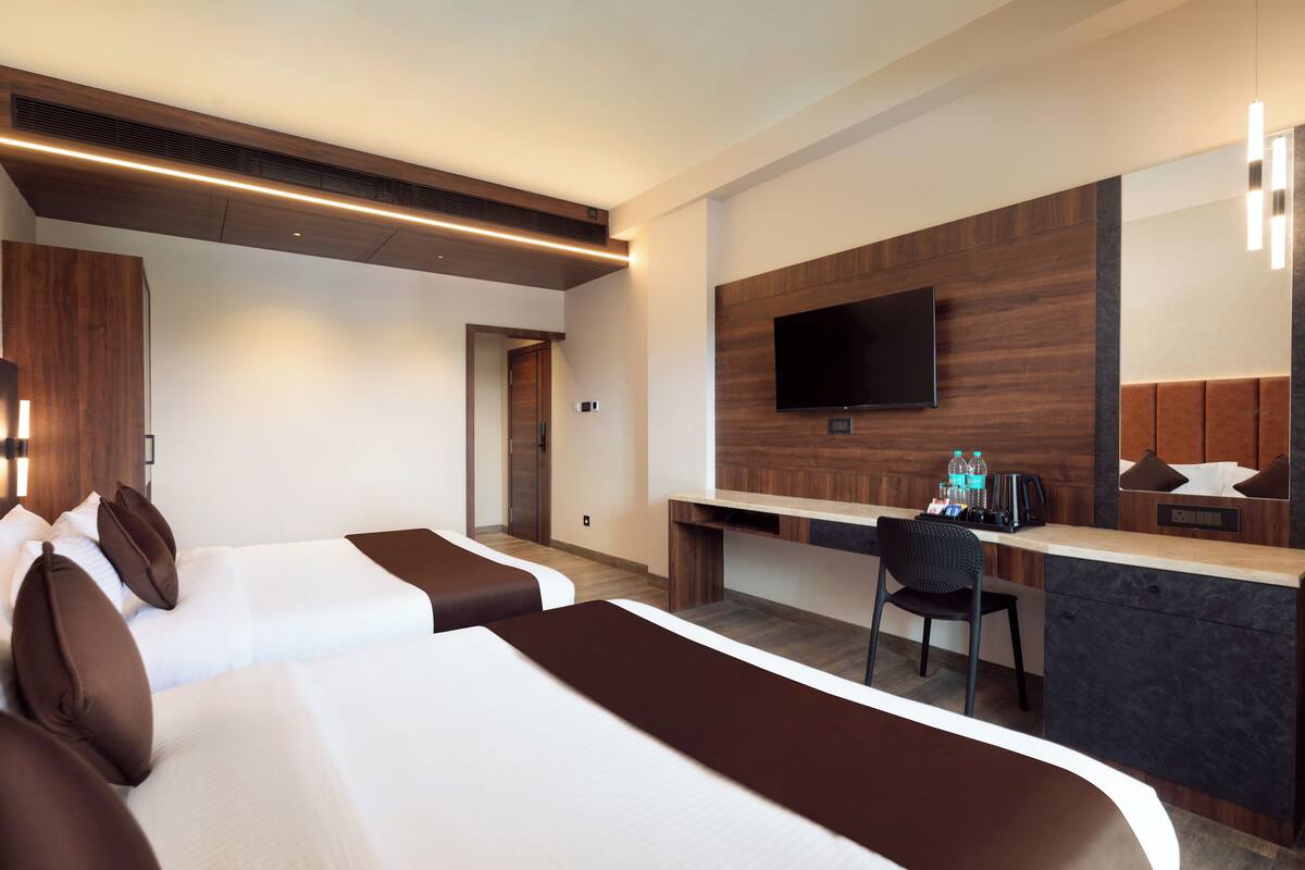 A hotel room with two beds, a desk, a chair, a TV, and a minibar.