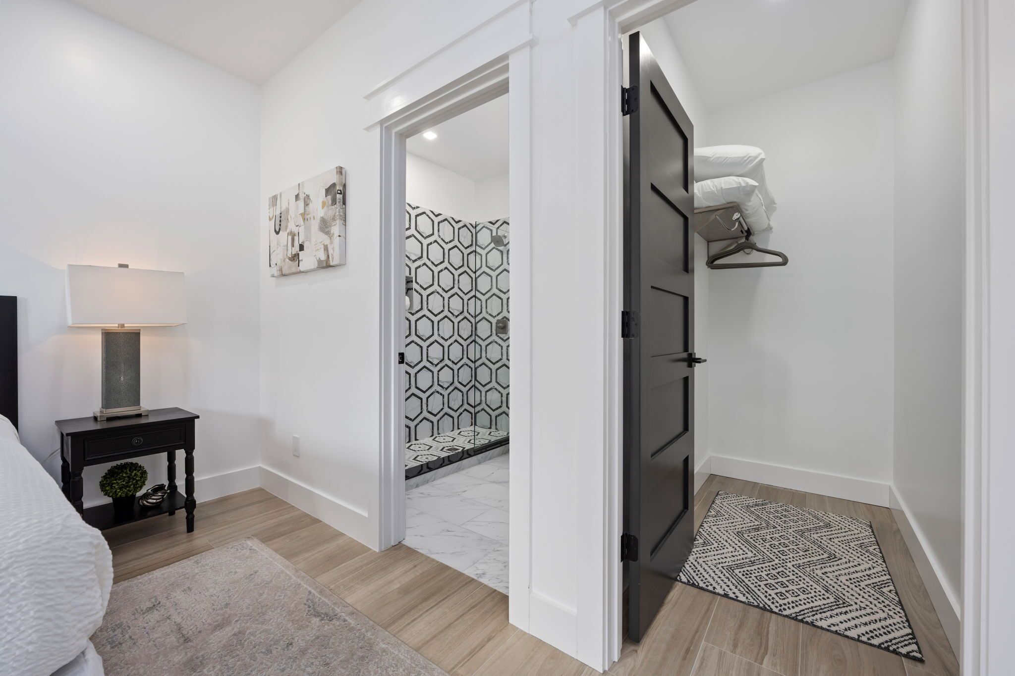 Un dormitorio moderno con cama, mesita de noche, lámpara y vistas a un baño con azulejos estampados.