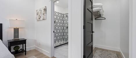 Un dormitorio moderno con cama, mesita de noche, lámpara y vistas a un baño con azulejos estampados.