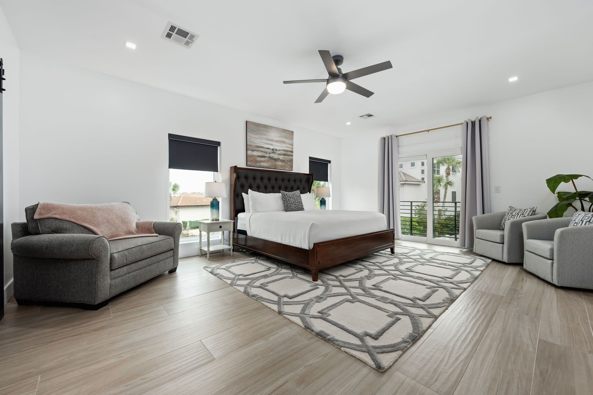 A modern bedroom with a bed, two sofas, a ceiling fan, and a view of the outside.