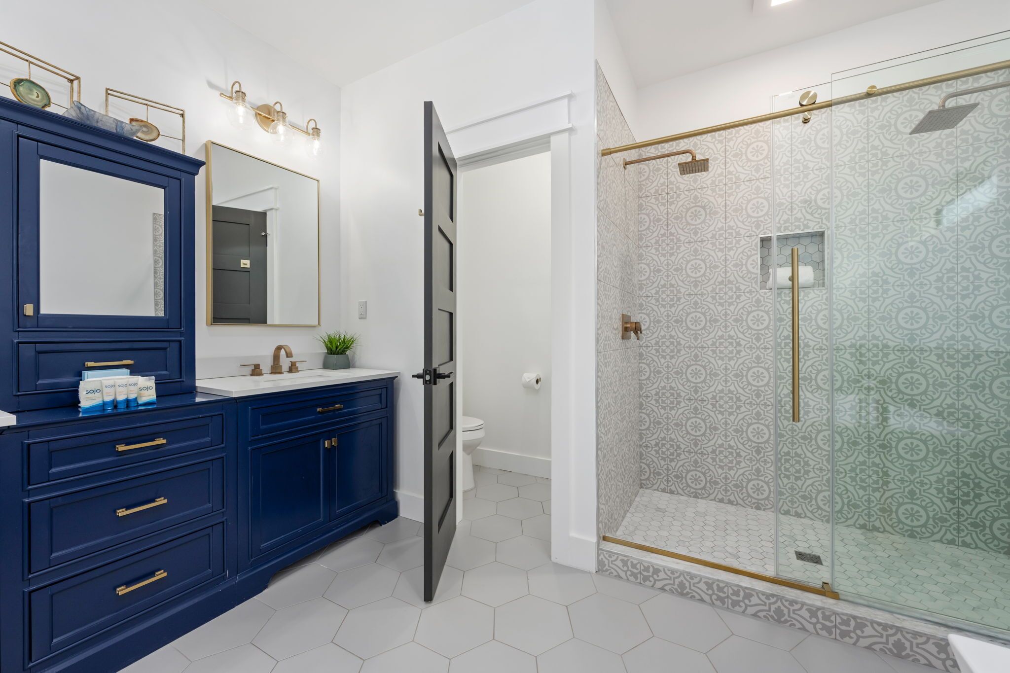 Een moderne badkamer met een blauwe wastafel, een grote spiegel, een douche met glazen wanden en een wit toilet.