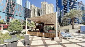 An outdoor patio area with a covered seating area, lounge chairs, and a checkered floor. - Bay Central West - Spacious Studio in the Dubai Marina (Dubai Marina)