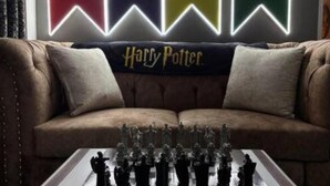 Une pièce avec un canapé marron, une couverture aux motifs de Harry Potter et un jeu d’échecs.