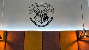 Une chambre à coucher avec un lit, des oreillers et un blason de Poudlard accroché au mur.