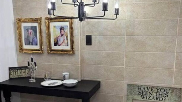 Une salle de bain avec un meuble-lavabo noir, un lustre, des tableaux encadrés et un panneau décoratif au mur.