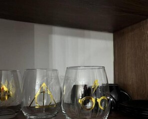 Trois verres ornés de symboles dorés, posés sur une étagère.