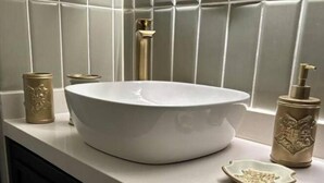 Une salle de bain avec un lavabo blanc, un robinet doré et un distributeur de savon doré assorti.