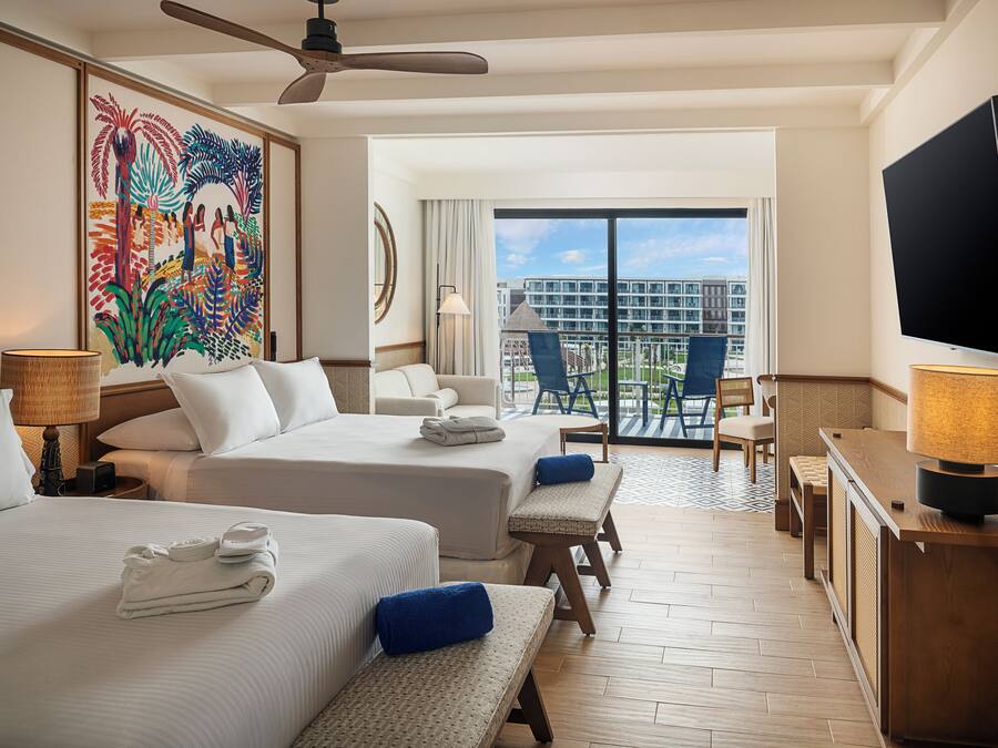 A hotel room with two beds, a balcony with a view of the city, a flat-screen TV, and a painting on the wall.
