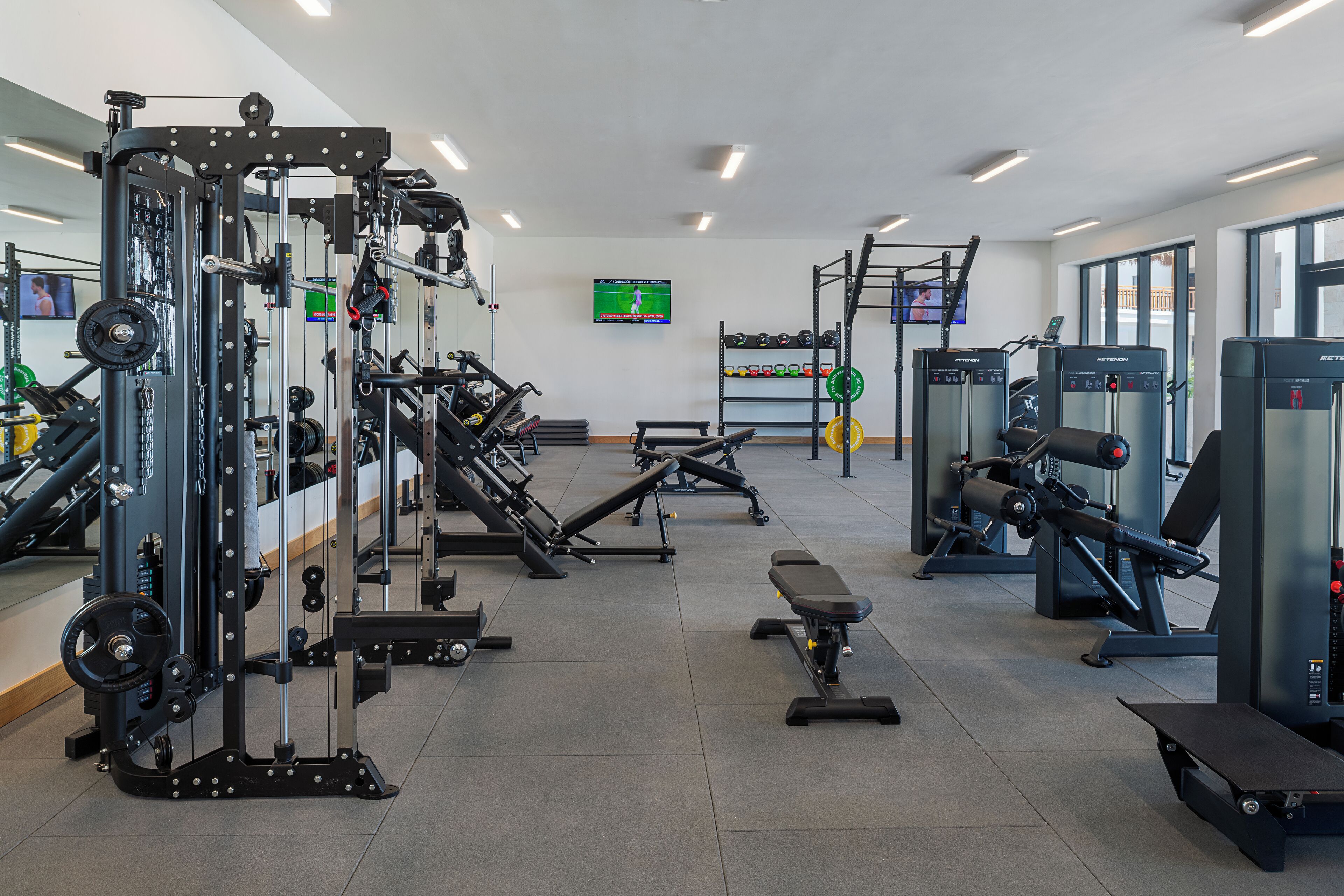 Un gimnasio con equipo de ejercicio diverso, una pantalla de televisión y un soporte para pesas.