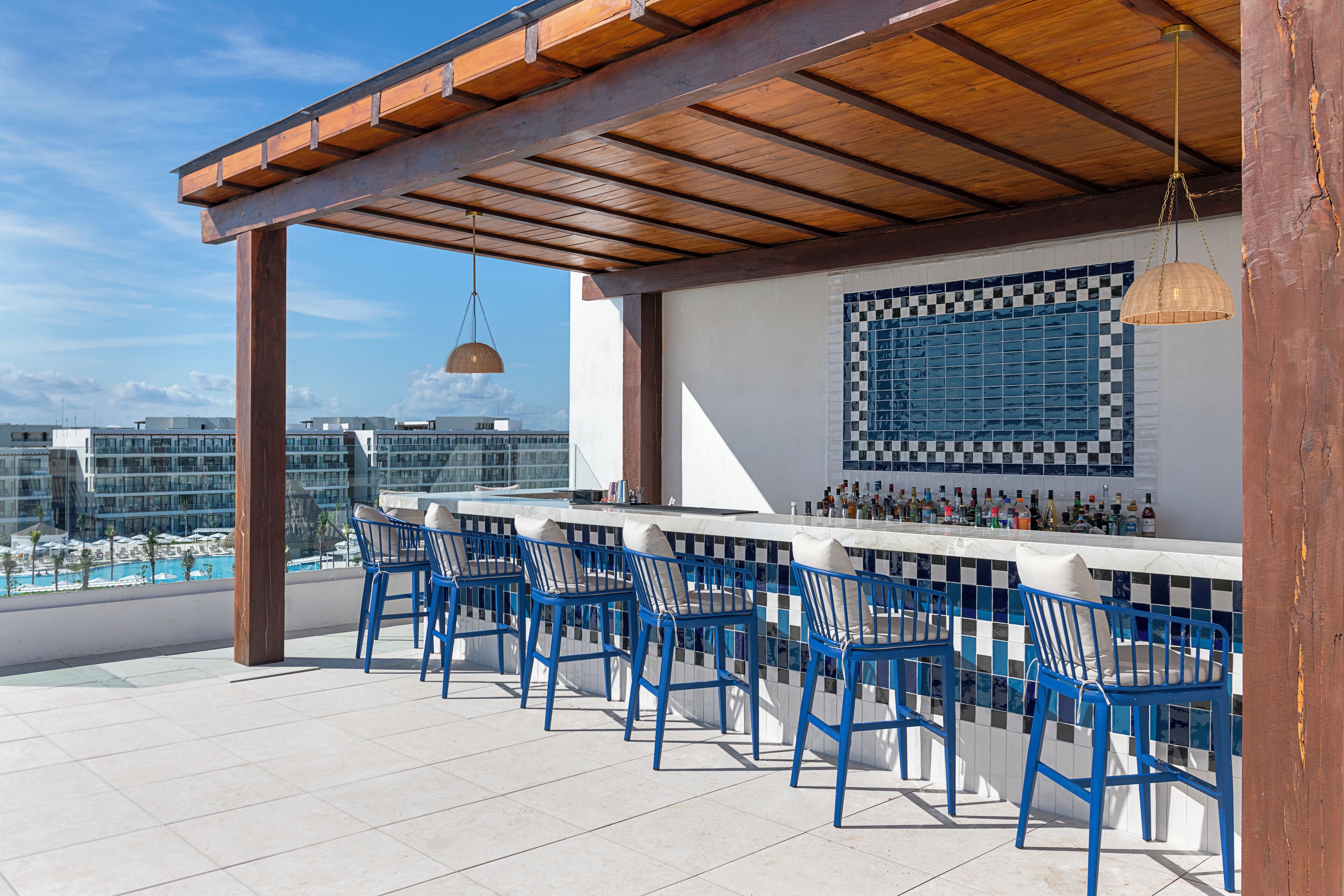 A rooftop bar with blue chairs and a checkered tile backsplash.