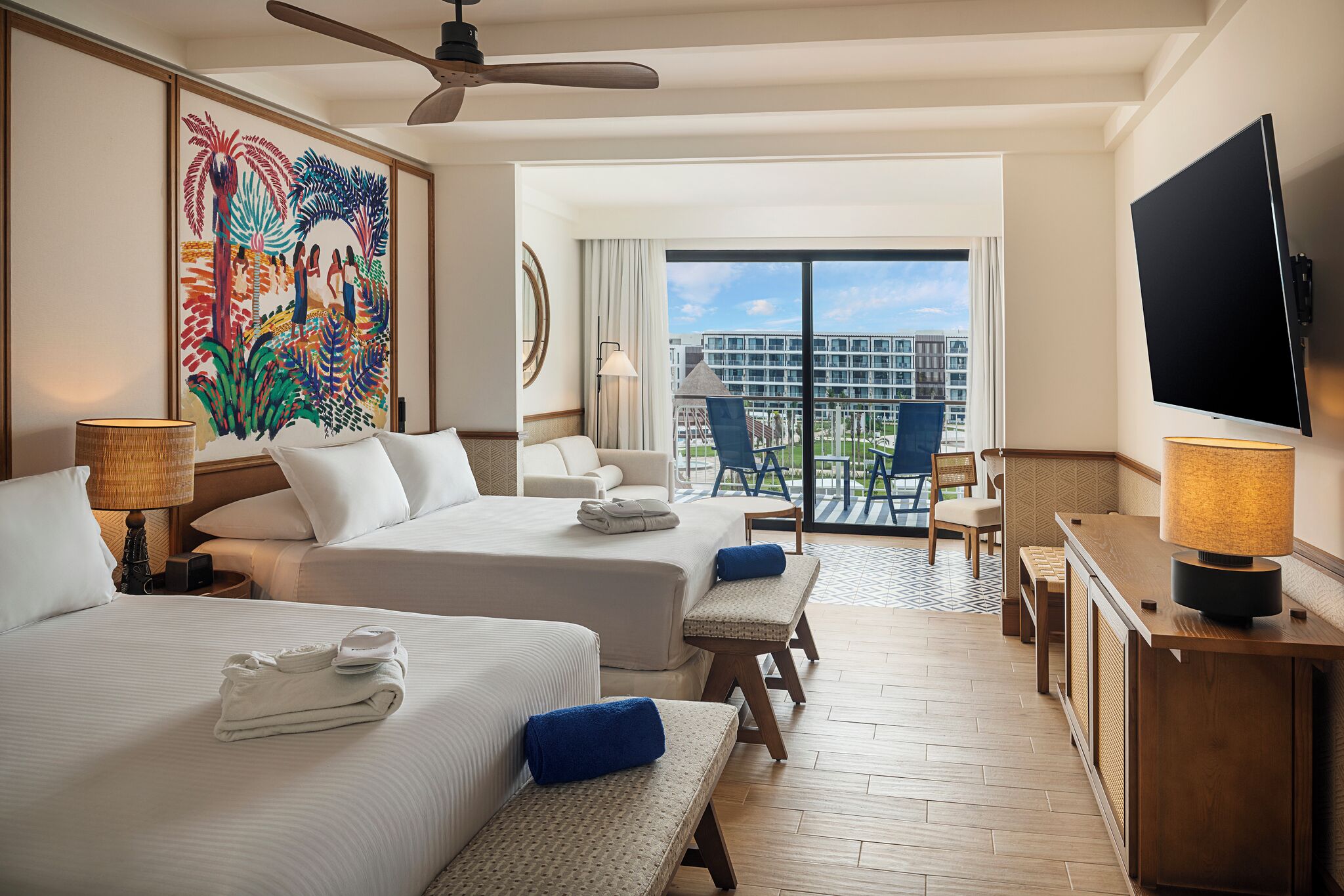 A hotel room with two beds, a balcony with a view, a TV, and a painting on the wall.
