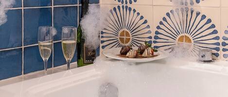A bathtub with a champagne bottle, glasses, and chocolate-covered strawberries.