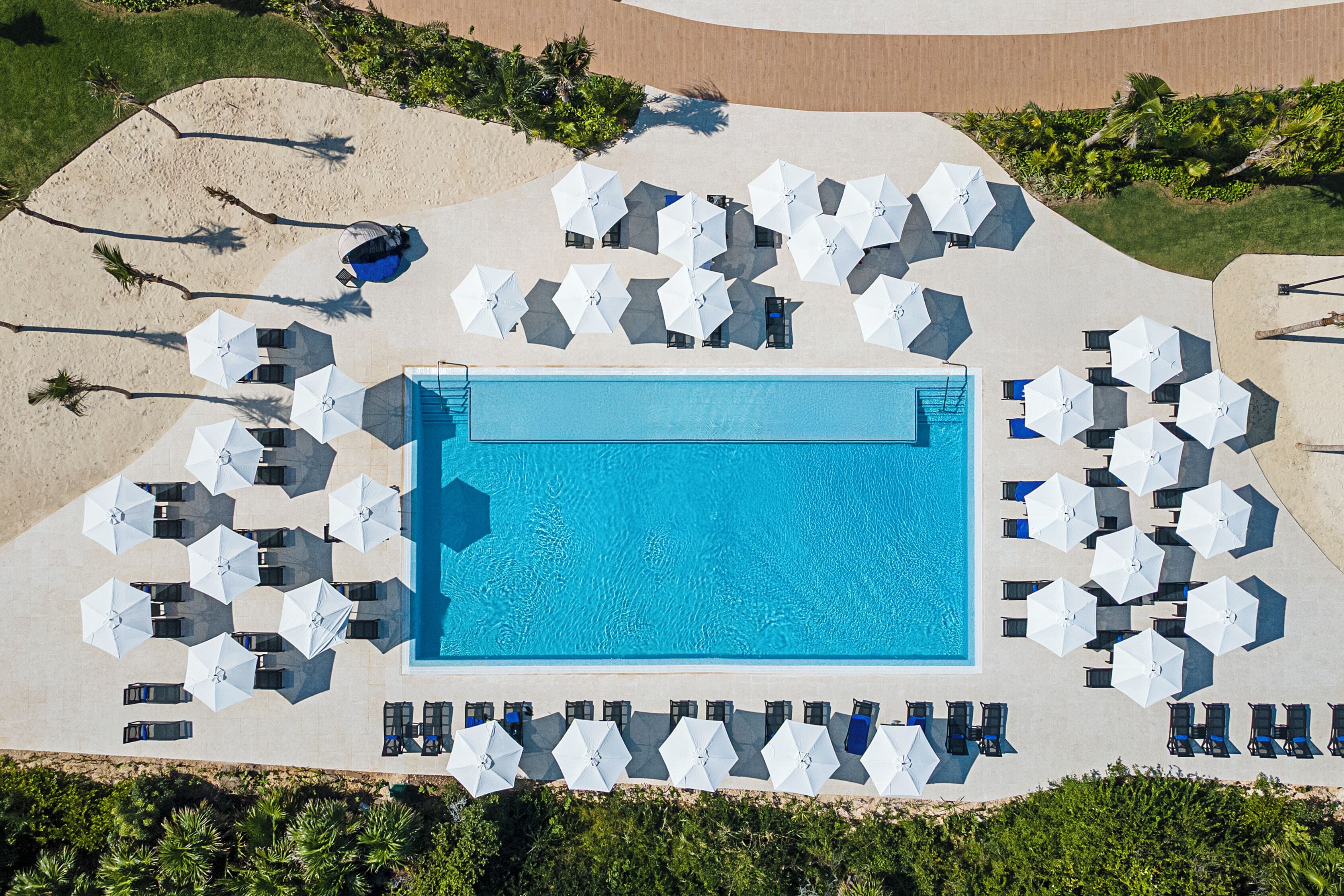 An aerial view of a pool area with multiple white umbrellas and lounge chairs arranged around a central pool.