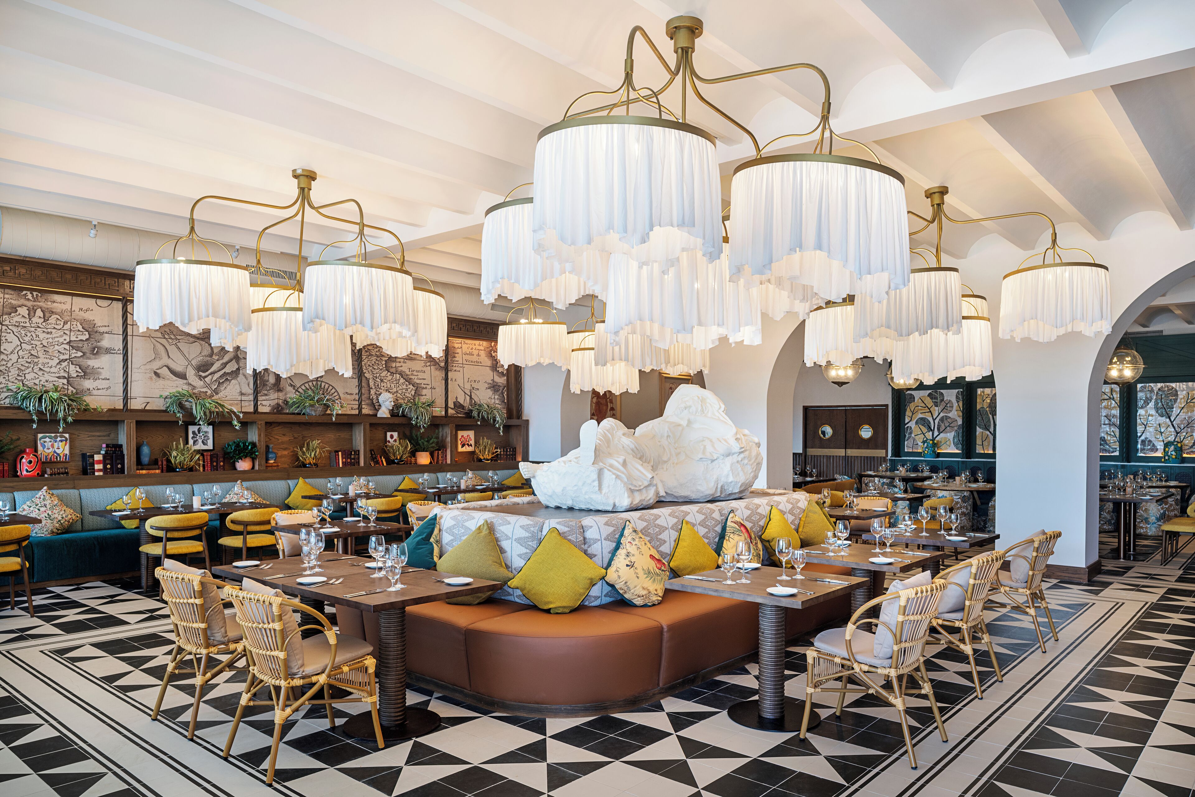 A spacious dining area with a central seating arrangement, multiple chandeliers, and a patterned floor.