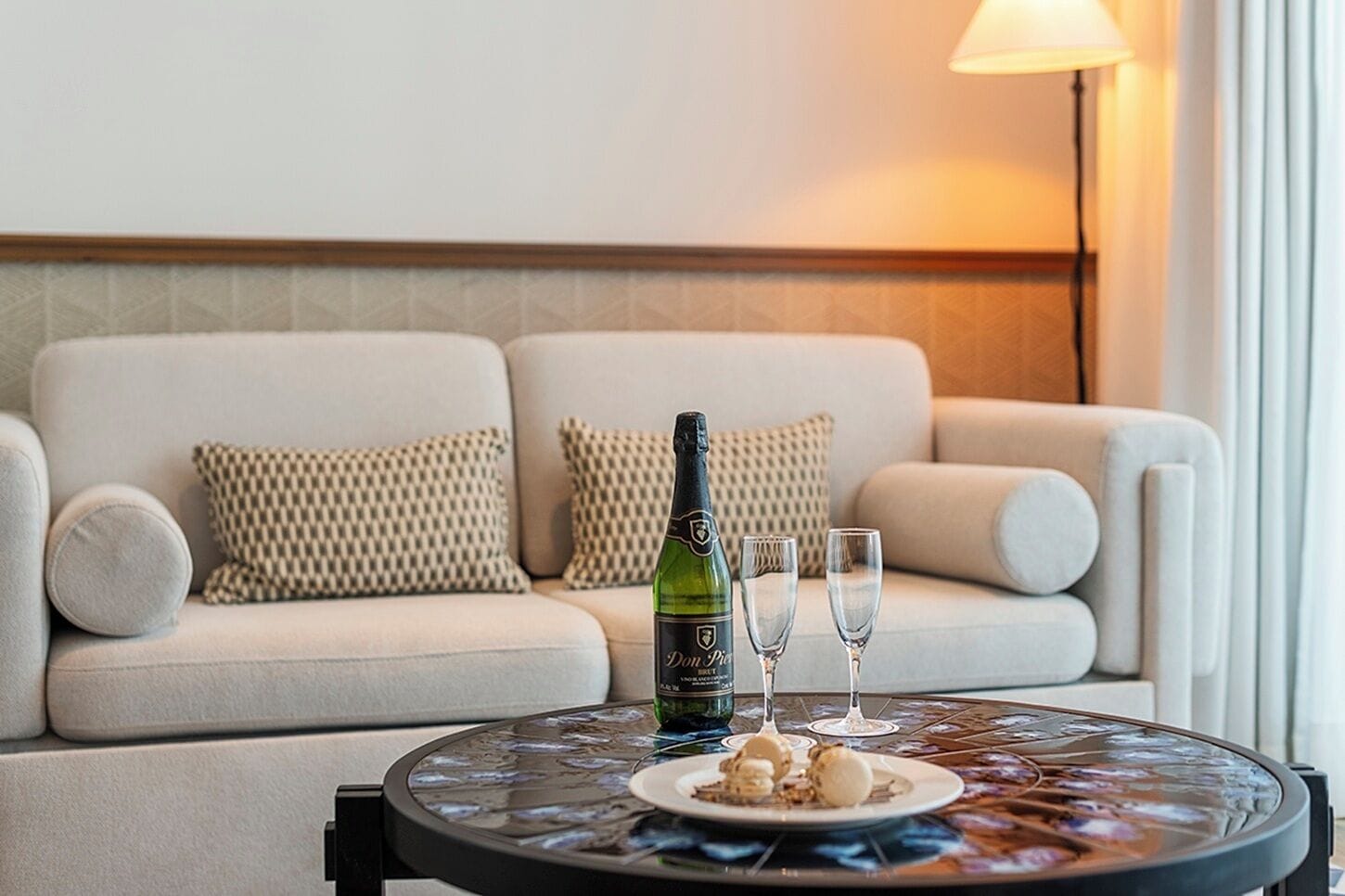 Una sala de estar moderna con un sofá, una mesa de centro de vidrio, una botella de champán, dos copas y un plato de comida.