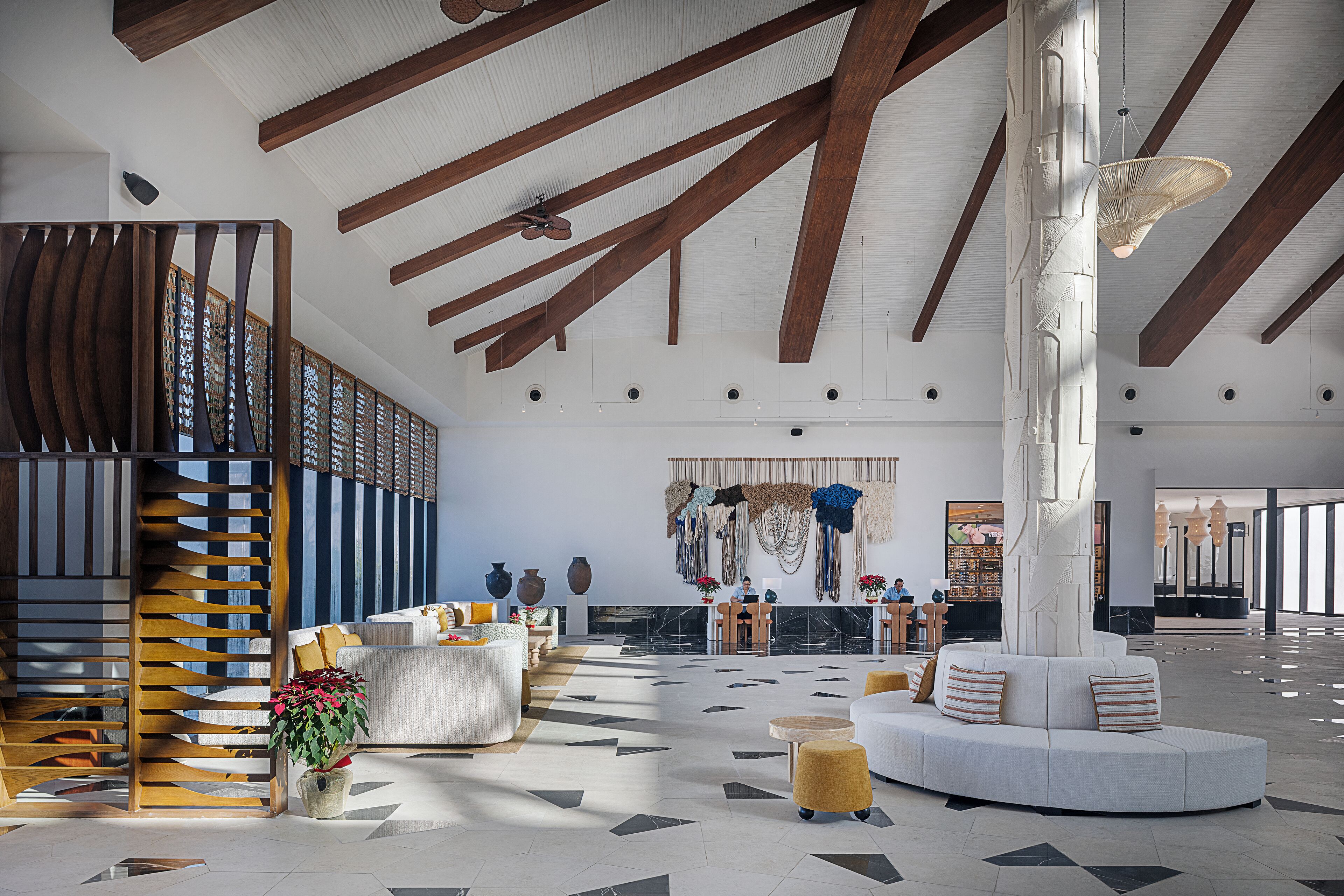 A spacious lobby with a high ceiling, wooden beams, a central white pillar, and a seating area with a sofa and ottoman.