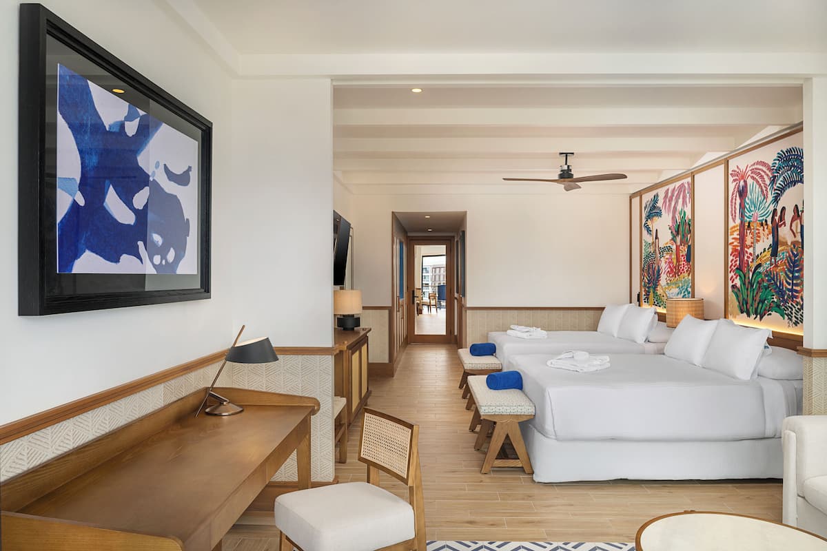 Habitación de hotel con una cama grande, un escritorio, una silla, un televisor y obras de arte en las paredes.