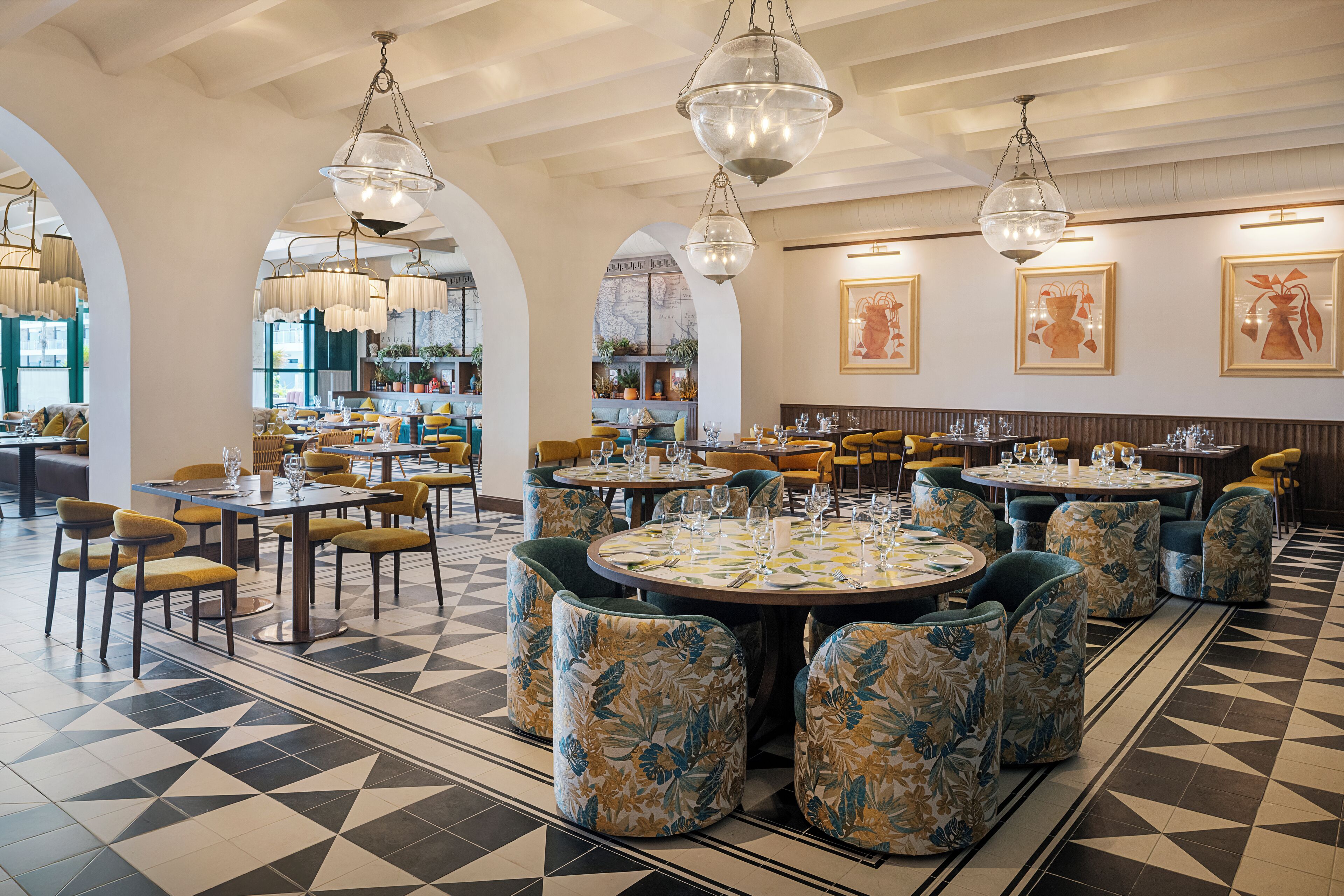 A restaurant with round tables, chairs, and hanging chandeliers.