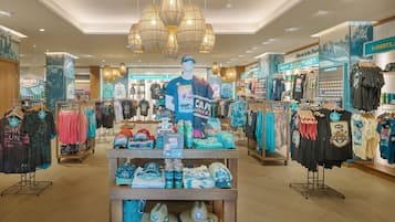 Uma loja de roupas com diversos artigos de vestuário e acessórios, incluindo chapéus e camisetas, expostos em araras e prateleiras.