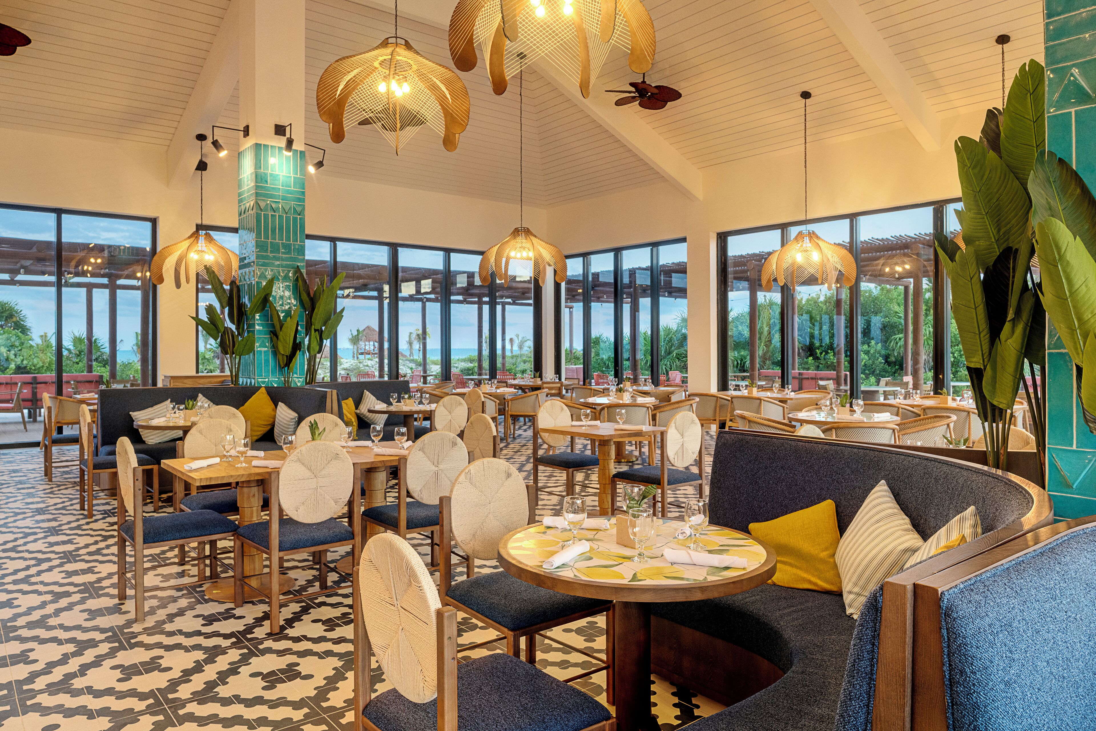 Un restaurante amplio con techos altos, ventanas grandes y diversas opciones de asientos, incluyendo mesas redondas y un sofá curvo.