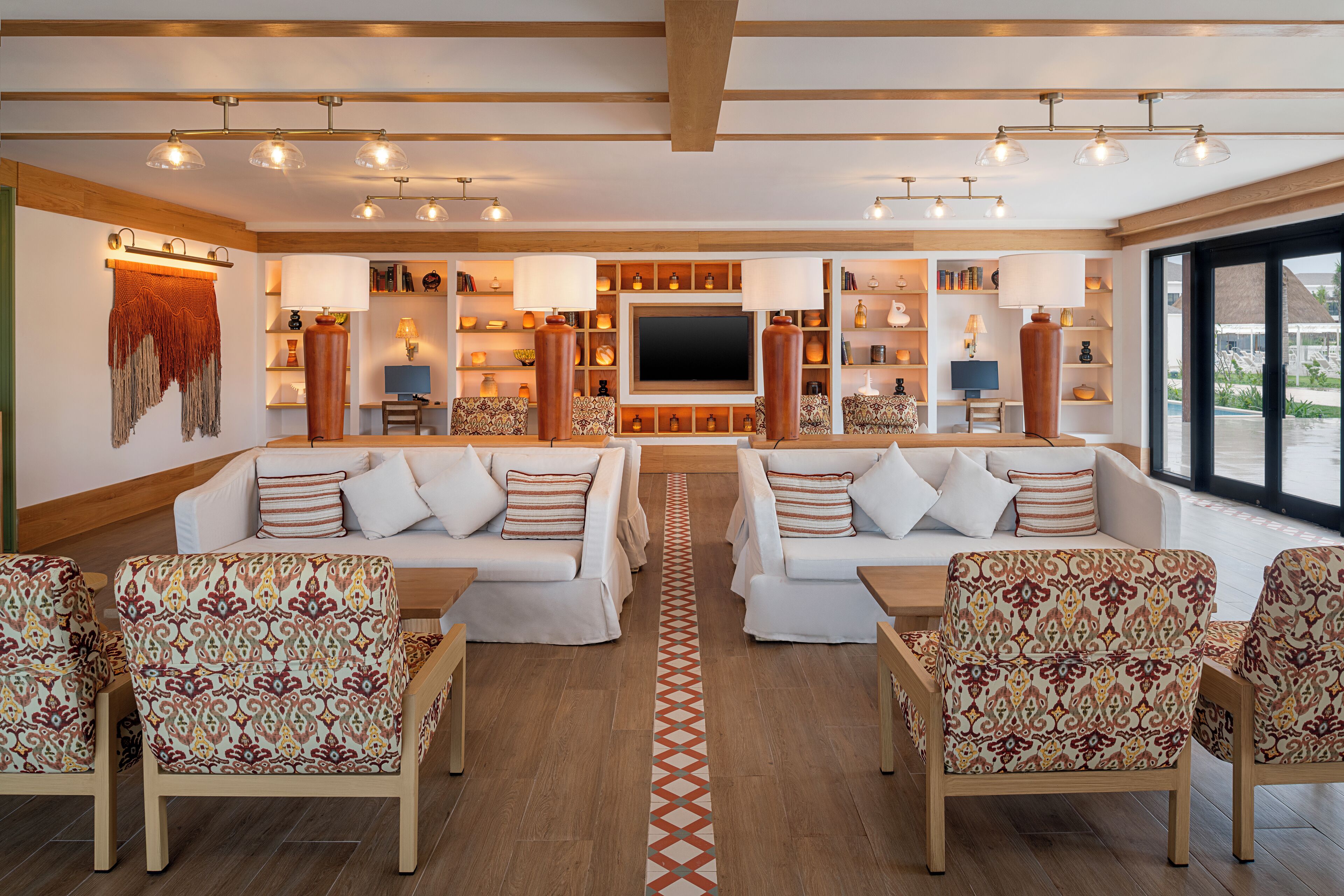 A spacious living area with two sofas and patterned chairs, a central rug, and a large TV.