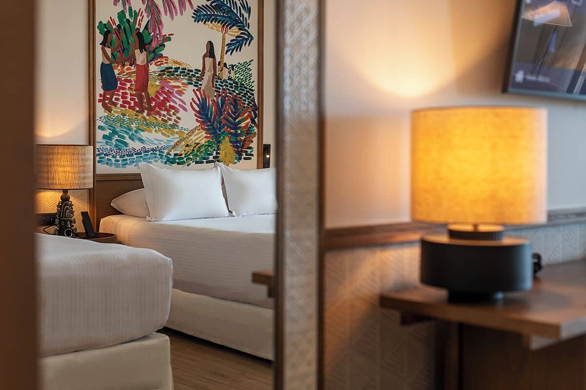 Habitación de hotel con cama, mesita de noche con lámpara, un cuadro en la pared y suelo de madera.