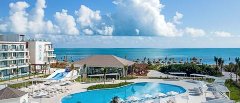 A resort with a large pool, sun loungers, a water slide, and a view of the ocean.