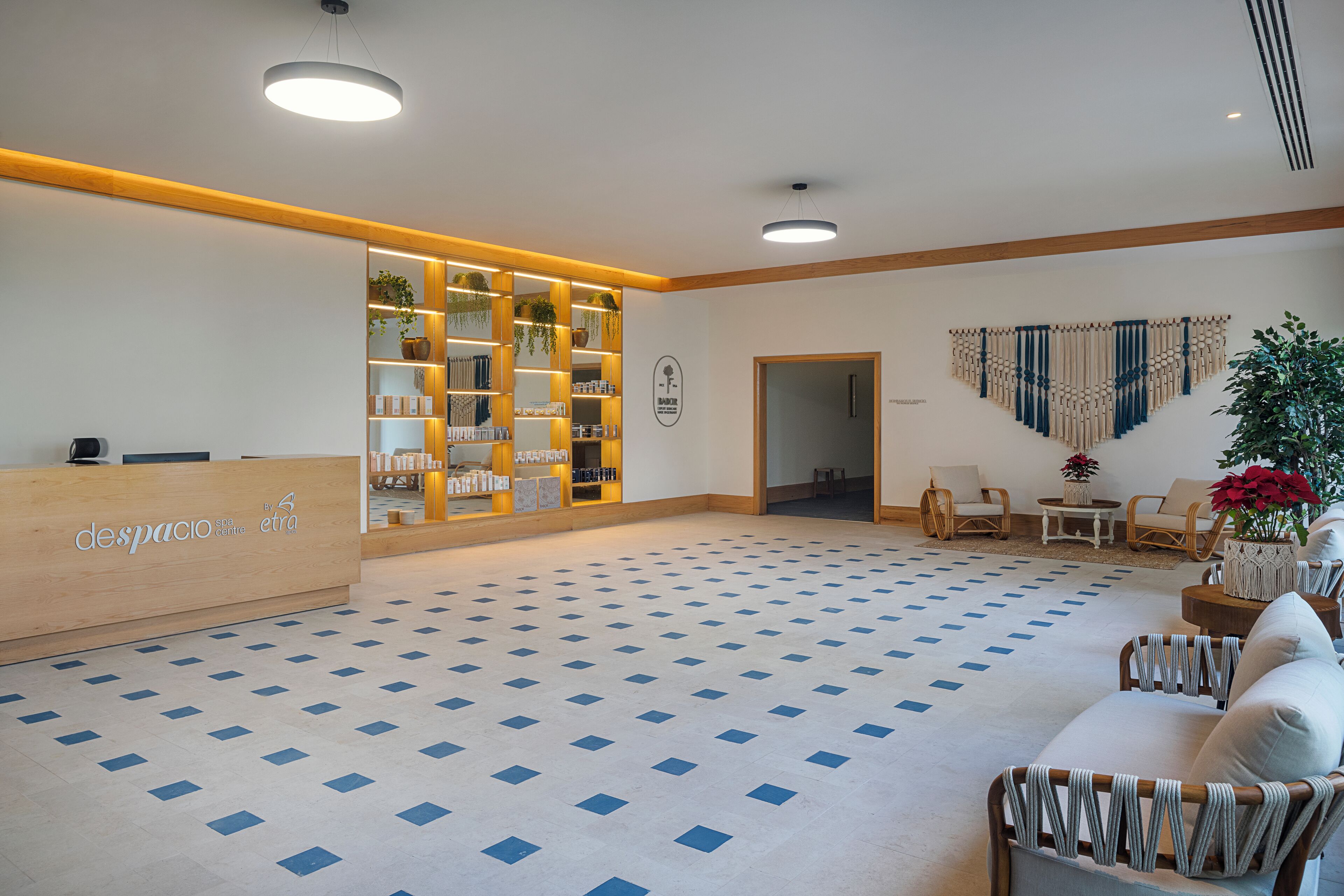 Zona de recepción con mostrador de registro, suelo estampado y área de descanso con sillas y una mesa.