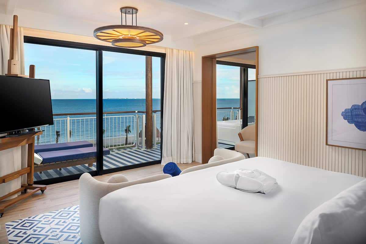 Una habitación de hotel con una cama grande, un televisor, un balcón con vistas al mar y un cuadro en la pared.