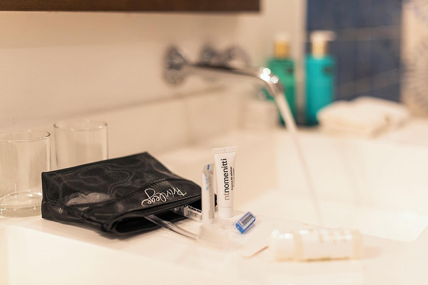 A bathroom with a sink, a black toiletry bag, a tube of cream, and a blue battery.