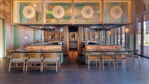 Un restaurante moderno con varias zonas de comedor, una barra central y vistas a la ciudad.