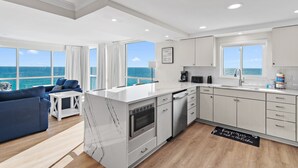 A modern kitchen with white cabinets, a built-in oven, and a dishwasher. There is a large window offering a view of the ocean. - 🌅 Gulf Front + Seasonal Comp Beach Setup | Shoreline 1081 - Stunning Views (Destin)