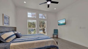 Un dormitorio con una cama, ventilador de techo, ventana y una silla.