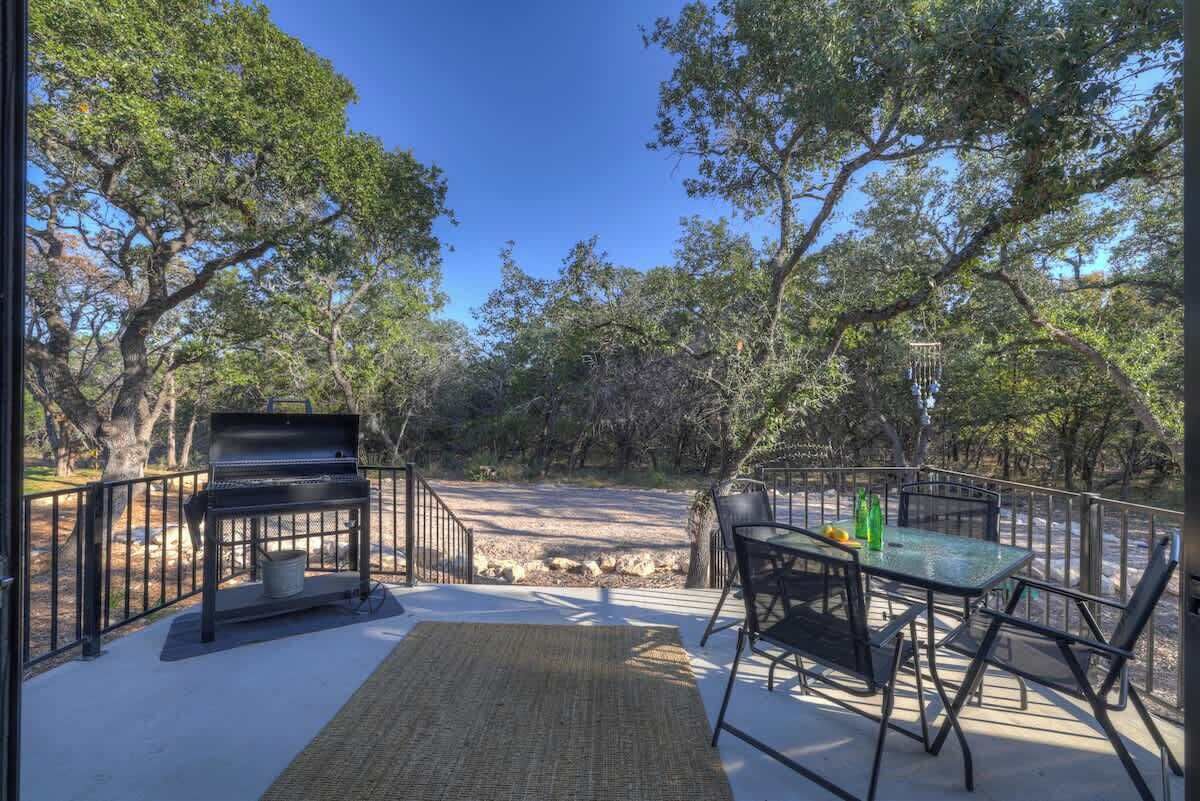 Un patio al aire libre con una parrilla, una mesa con sillas y vistas a un área boscosa.