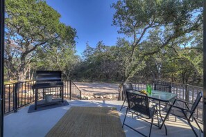 An outdoor patio with a grill, a table with chairs, and a view of a wooded area.