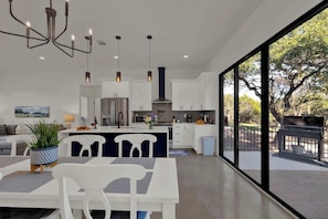 A modern kitchen with white cabinetry, a stainless steel refrigerator, and a dining area with a white table and chairs. - Serene Guadalupe Getaway-River Access Nearby! (Spring Branch)