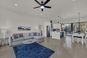 A modern living room with a gray sectional sofa, a blue rug, and a dining area with white furniture. - Serene Guadalupe Getaway-River Access Nearby! (Spring Branch)