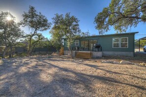 A single-story house with a covered porch, a small deck, and a gravel driveway. - Serene Guadalupe Getaway-River Access Nearby! (Spring Branch)