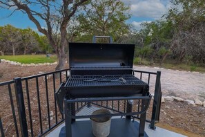 Un barbecue portable doté d’un couvercle en treillis et d’une poignée, placé sur une surface en béton et entouré d’une rambarde métallique.