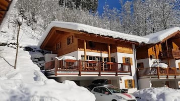 Um chalé de madeira com varanda, rodeado por árvores cobertas de neve.