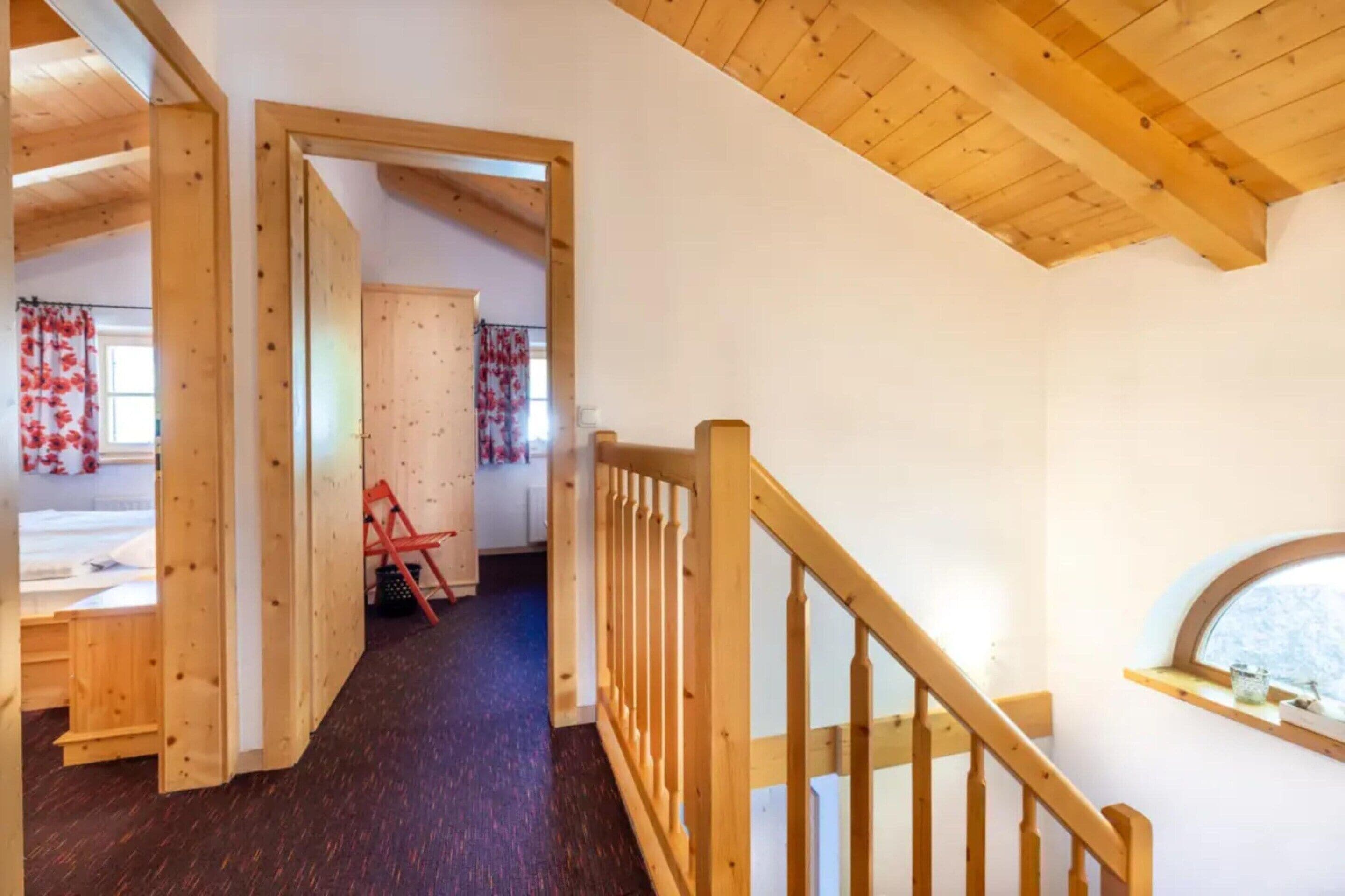 A wooden staircase leading to a lofted room with a window, a door, and a chair.