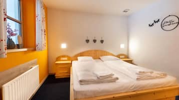 Quarto de hotel com cama de madeira, mesa de cabeceira, penteadeira, janela com cortinas e um adorno na parede.