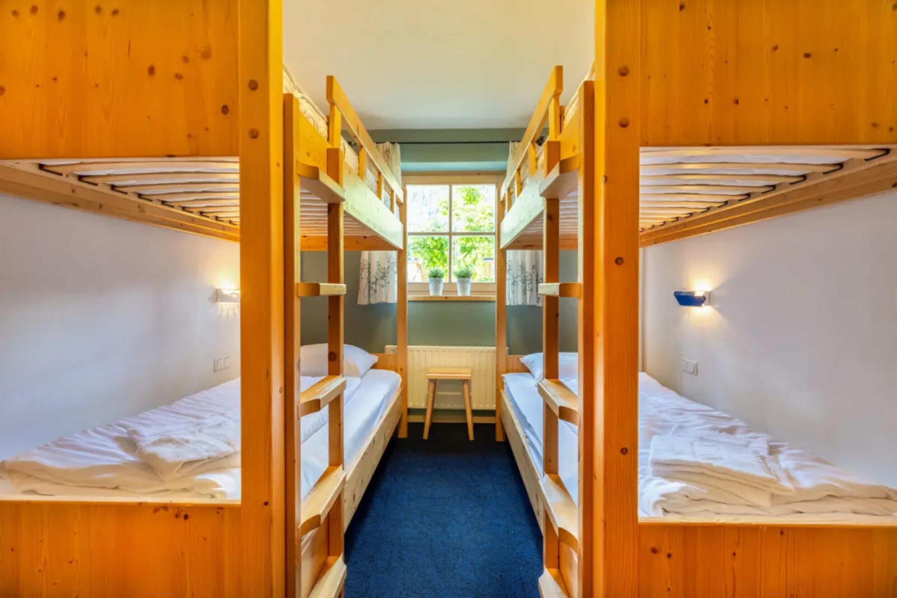 Ein Zimmer mit Etagenbetten, einem kleinen Tisch und einem Fenster mit Blick auf Grünflächen.